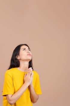 Caucasian woman looking up while praying with folded hands in studio with brown background