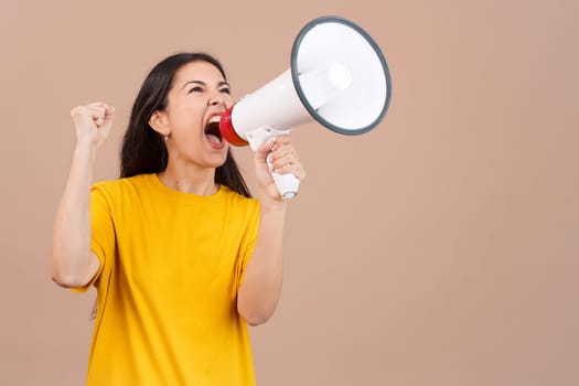 Upset caucasian woman yelling using a loudspeaker in studio with brown background