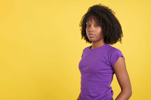 Serious woman with afro hair looking at camera in studio with yellow background