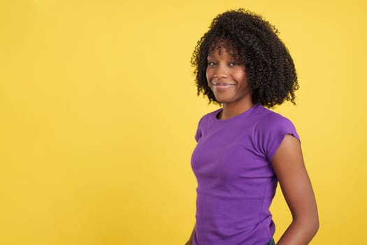 Proud woman with afro hair standing smiling at camera in studio with yellow background
