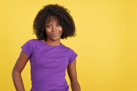 Woman with afro hair smiling at camera in studio with yellow background
