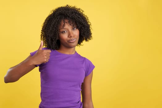 Woman with afro hair gesturing approval with the thumb up in studio with yellow background