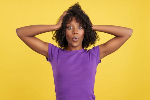 Cool woman with afro hair expressing surprise in studio with yellow background