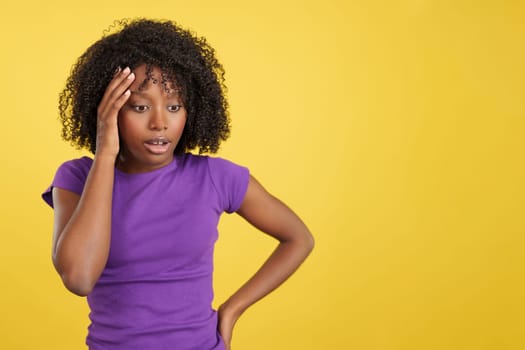 Woman with African hair gesturing that she is forgetting something in studio with yellow background