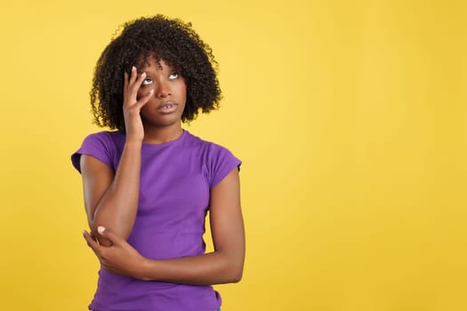 Bored woman with afro hair looking up in studio with yellow background