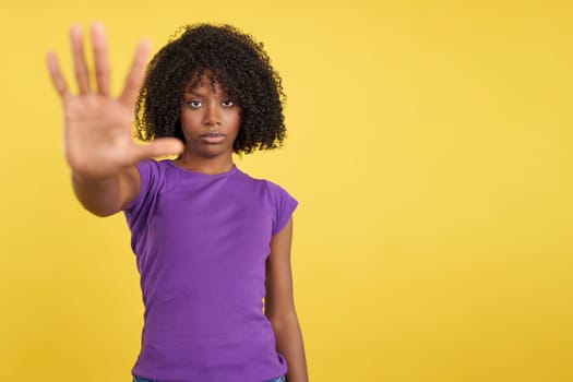 Woman with African hair gesturing rejection in studio with yellow background
