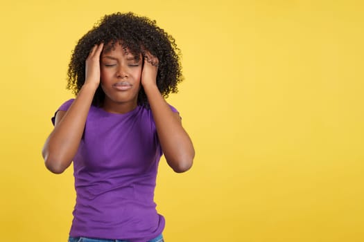 Woman with afro hair standing with headache in studio with yellow background