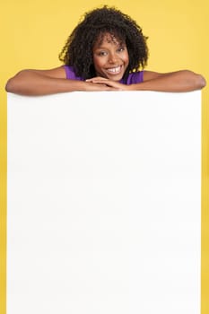 Happy woman with afro hair above a blank panel in studio with yellow background