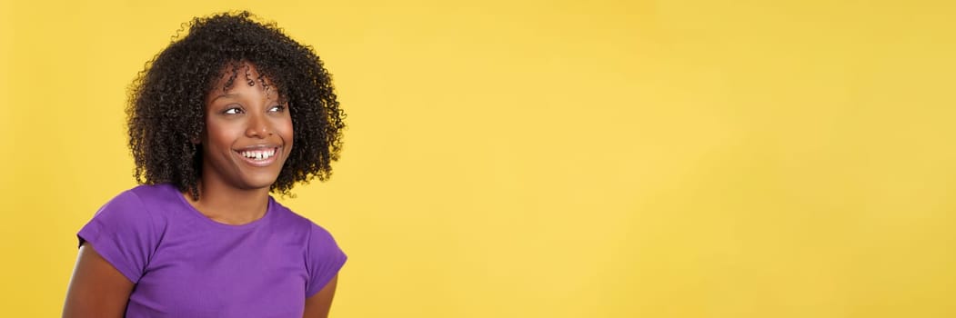 Cool woman with afro hair looking aside to a blank space in studio with yellow background