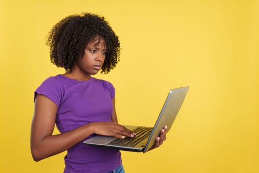 Worried woman with afro hair using a laptop in studio with yellow background