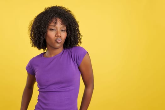 Provocative woman with afro hair kissing at camera in studio with yellow background