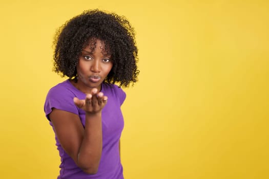 Sensual african woman blowing a kiss while looking at camera in studio with yellow background