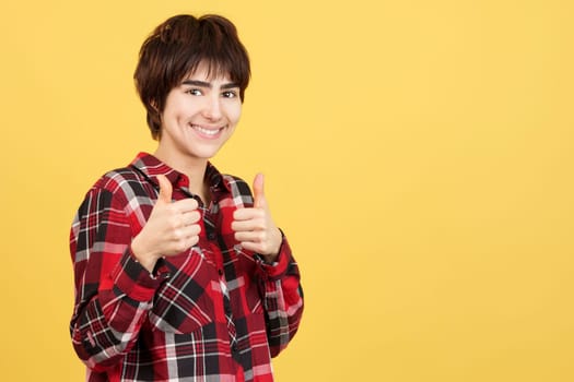 Androgynous person gesturing approval with the thumbs up in studio with yellow background