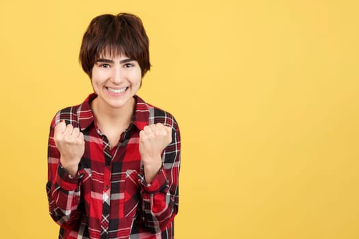 Androgynous person celebrating while raising the fists in studio with yellow background