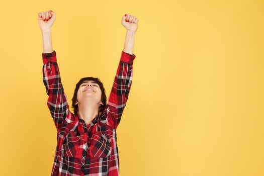 Happy androgynous person celebrating with arms up in studio with yellow background