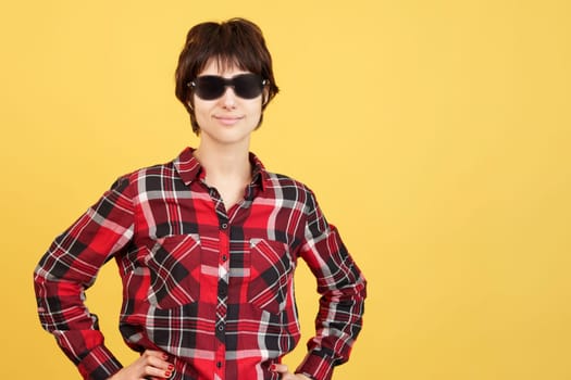 Cool Androgynous person standing looking at camera with sunglasses in studio with yellow background