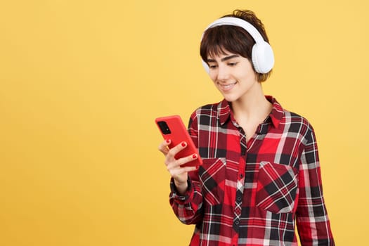 Androgynous person listening to music with mobile and headphones in studio with yellow background