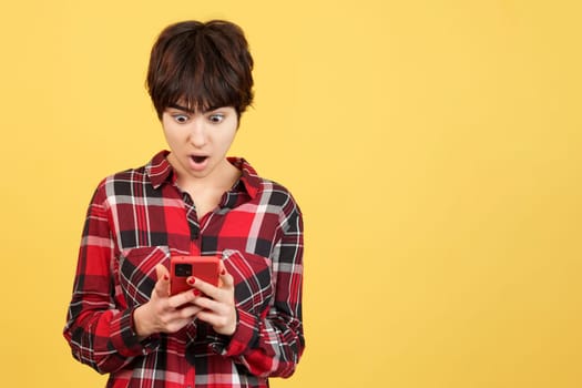 Androgynous person looking at the mobile with surprised expression in studio with yellow background