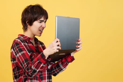 Worried androgynous person standing while using a laptop in studio with yellow background