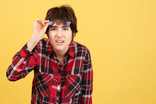 Androgynous person taking off her glasses to look ahead in studio with yellow background