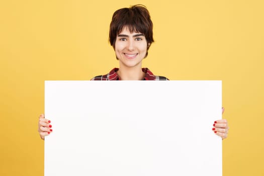 Androgynous person holding a blank panel while smiling in studio with yellow background