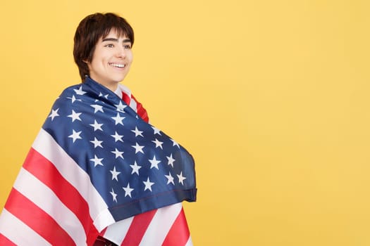 Androgynous person wrapped with a USA flag in studio with yellow background