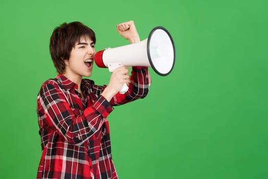 Androgynous person yelling while using a megaphone in studio with green background