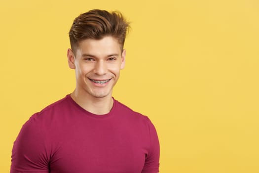 Caucasian man smiling while wearing brackets on his teeth in studio with yellow background