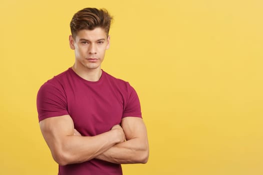 Serious man looking at camera with arms crossed in studio with yellow background