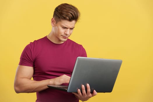 Strong man having a problem while using a laptop in studio with yellow background