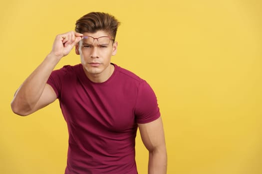 Strong man taking off her eyeglasses to see ahead in studio with yellow background