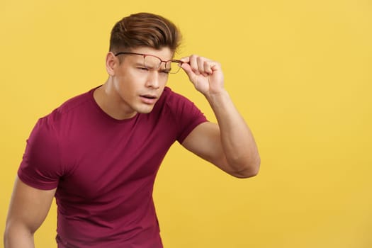 Strong man taking off her glasses to see far away in studio with yellow background