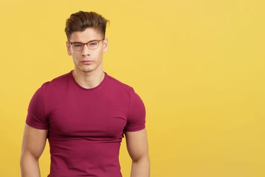 Attractive student with eyeglasses looking at camera in studio with yellow background