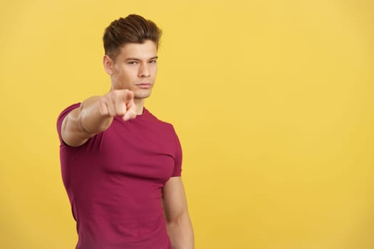 Handsome caucasian man pointing to camera with index finger in studio with yellow background