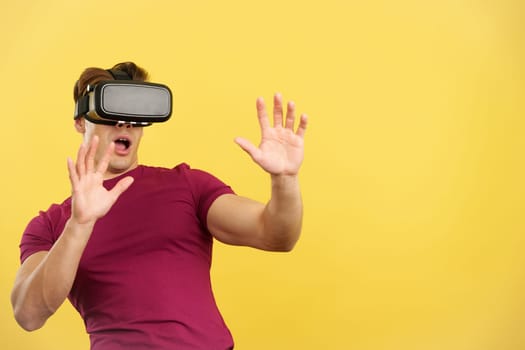 Surprised strong man with Virtual Reality goggles in studio with yellow background