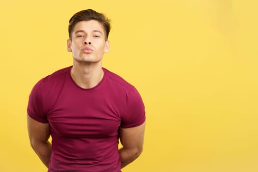 Sensual and strong man kissing while looking at camera in studio with yellow background