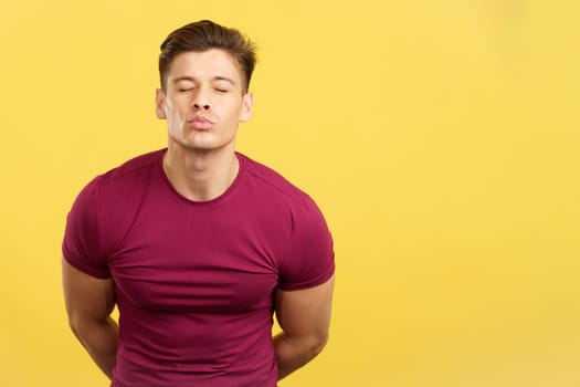 Provocative strong handsome man kissing at camera in studio with yellow background