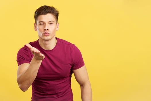 Man blowing a kiss while looking at the camera in studio with yellow background