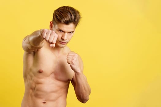 Strong shirtless man doing shadow boxing while looking at camera in studio with yellow background