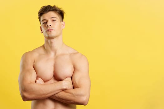 Proud strong man looking at camera shirtless in studio with yellow background