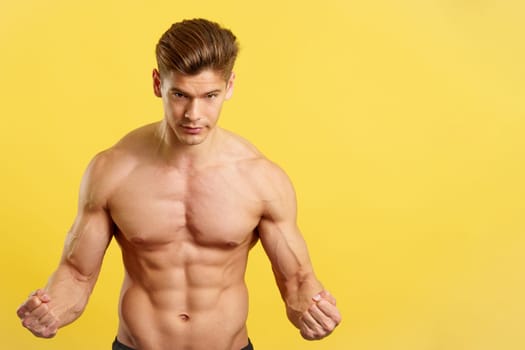 Strong man with abs looking at camera showing muscle in studio with yellow background