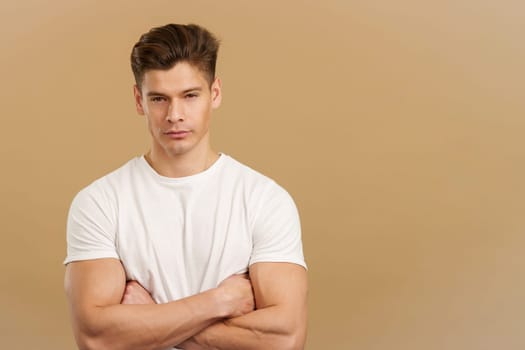 Proud strong man looking at camera with arms folded in studio with brown background