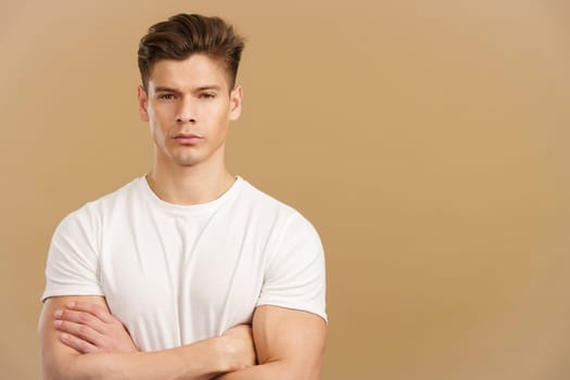 Handsome man crossing the arms while looking the camera with an angry expression in studio with brown background