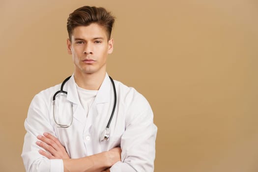 Handsome serious doctor looking at camera standing with arms crossed in studio with brown background