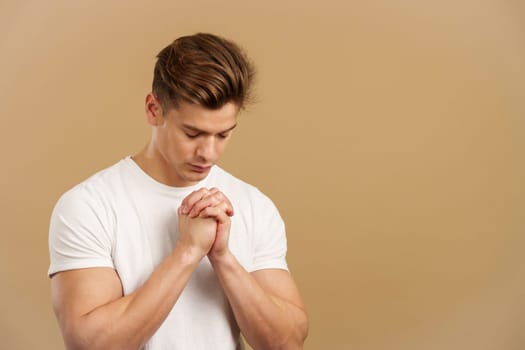 Man praying with the hands together looking down in studio with brown background