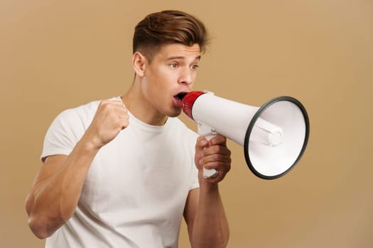 Upset caucasian man yelling using a loudspeaker in studio with brown background