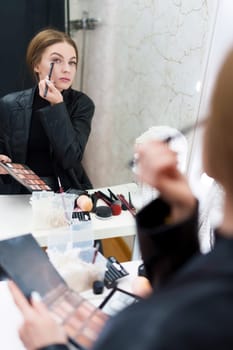 Reflection on a mirror of a woman applying eye shadow while making up in a backstage