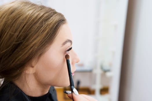 Close up portrait of the profile of a woman applying eye shadow on a backstage