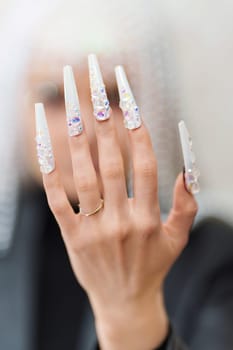 Vertical photo of the hand of a woman with white and long fake nails