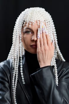 Studio portrait with back background of a woman with wig of pearls covering one eye with hand